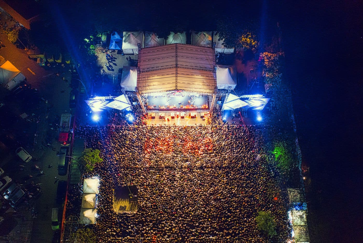 Vue aérienne d'un concert en plein air, la nuit : une scène éclairée et une foule dense devant elle